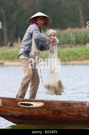 Pescatore vietnamita pronto a gettare la sua mano-net da una piccola barca in modo tradizionale Foto Stock