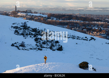 Walker in cerca di neve oltre a Calton Hill da Arthur' Seat in Holyrood Park, Edimburgo, Scozia Foto Stock