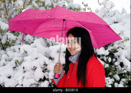 Giovane donna con colore rosso brillante cappotto e ombrello rosa a piedi nella neve fresca Foto Stock