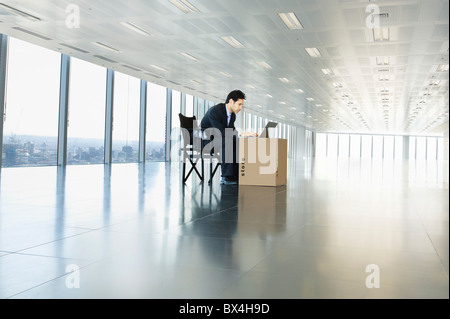 Imprenditore lavorando sul computer portatile in ufficio vuoto dello spazio mediante la scatola di cartone come desk Foto Stock