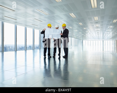 Tre dirigenti in hardhats guardando i piani in vuoto spazio in ufficio Foto Stock