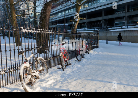 Biciclette parcheggiate in ringhiere nella neve con le principali università della libreria di Edimburgo, Scozia Foto Stock