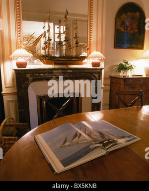 Libro pittorico aperto sulla tavola in una tradizionale sala da pranzo con lampade illuminate su entrambi i lati del Modello di nave su mantelpiece Foto Stock