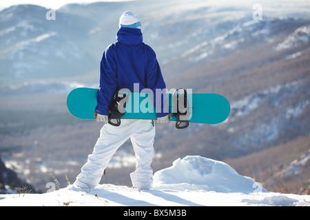 Vista posteriore di uno sportivo con lo snowboard in piedi sulla cima del monte Foto Stock