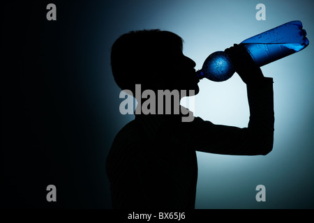 Silhouette di donna giovane acqua potabile dalla bottiglia su sfondo blu. Sagoma orizzontale, vista laterale, spazio di copia Foto Stock