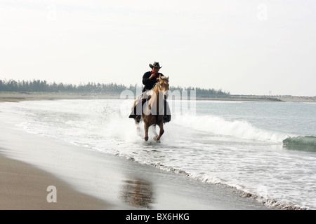 Un asiatico cavaliere corre il suo cavallo sulla spiaggia. Tainan, Taiwan Foto Stock