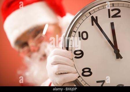 Foto di un orologio che mostra cinque minuti a mezzanotte con Santa sullo sfondo Foto Stock