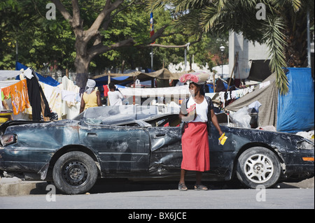 Donna di fronte a un'auto danneggiata, Gennaio 2010 terremoto, dal centro di Port au Prince, Haiti, West Indies Foto Stock