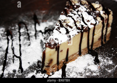 Una fetta di New York style cheesecake spruzzata con salsa di cioccolato Foto Stock