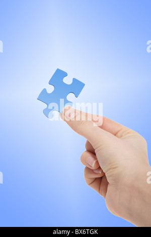 Una persona in possesso di un pezzo di colore blu di un puzzle nella sua mano nella parte anteriore di un bianco a gradiente blu. Foto Stock