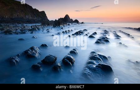 Alta Marea sommerge gradualmente le sponde rocciose di Blegberry Bay al tramonto, Hartland, Devon, Inghilterra. Estate (settembre 2010). Foto Stock