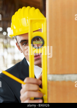 Architetto utilizza il livello sulla parete rossa nel sito in costruzione Foto Stock