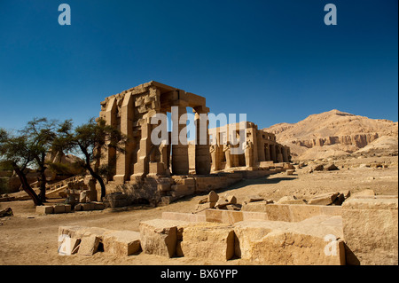 I pilastri e le statue di una rovina tempio egizio stand con orgoglio nel sole del mattino con la Valle dei Re dietro Foto Stock