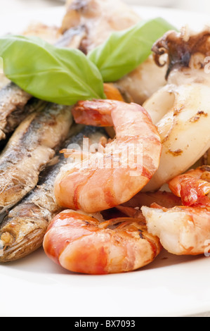 Pesce fritto con le acciughe e basilico come primo piano su una piastra bianca Foto Stock