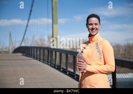 Una donna è in piedi su un ponte che tiene una bottiglia di acqua Foto Stock