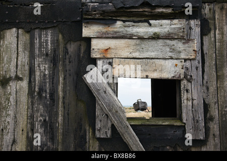 Aprire la finestra in una abbandonata e in disuso capanna di pescatori guardando verso una barca abbandonata a Dungeness Beach, Kent REGNO UNITO Foto Stock