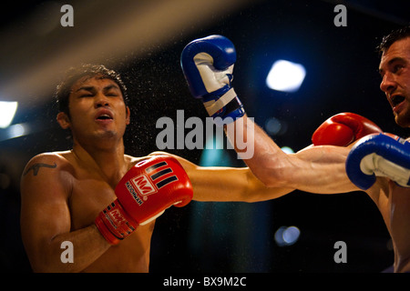 Combattente caucasica sbarco uppercut alla faccia del Thai boxer asiatici, sudore battenti durante outdoor amateur muay thai kickboxing match Foto Stock