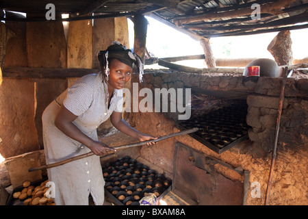Un baker (Rehama Mbabazi) mette il pane nel suo forno nel villaggio Mutukula, Iganga distretto, Uganda orientale, Africa orientale. Foto Stock
