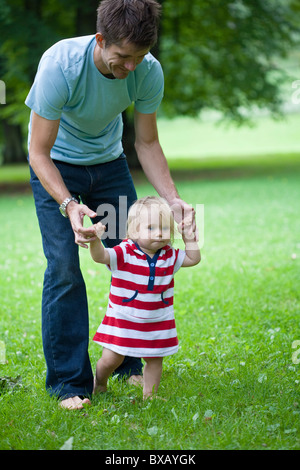 La metà degli adulti aiutando il padre figlia con i primi passi Foto Stock