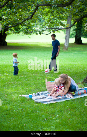 Madre libro di lettura per la figlia e il padre giocava a calcio con il figlio nel parco Foto Stock