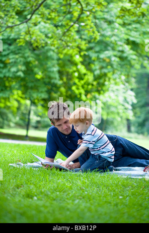Father reading book to son in park Foto Stock