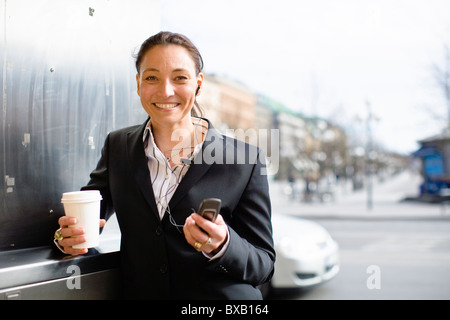 Ritratto di Allegro imprenditrice con pasti da asporto caffè in una mano e il telefono cellulare a un altro Foto Stock