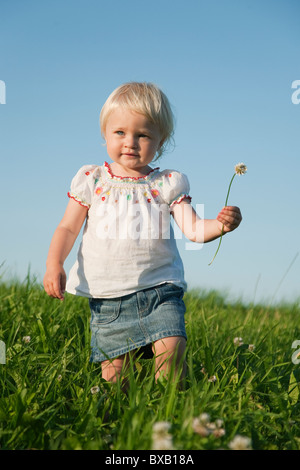 Ragazza con fiore e passeggiate attraverso prati Foto Stock