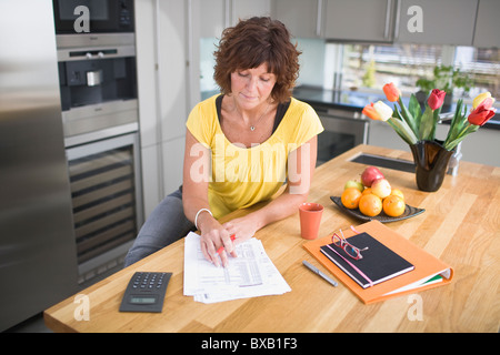 Donna seduta in cucina facendo di documenti cartacei Foto Stock