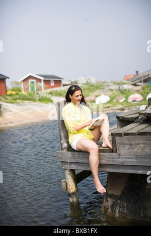 Donna seduta su un pontile e libro di lettura Foto Stock
