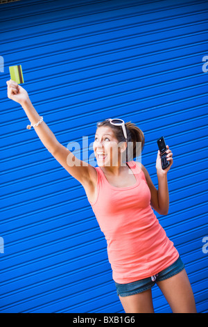 Giovane donna di fronte blu parete, mantenendo la carta di credito e telefono cellulare Foto Stock