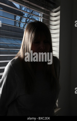 Ritratto di un anonimo bionda donna seduta con la schiena di una finestra in legno tenda alla notte. Foto Stock