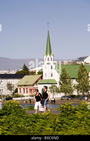 Due donne a piedi dal lago Tjornin, Frikirkjan chiesa in background. Reykjavik Islanda Foto Stock