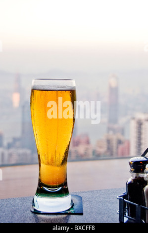 Bicchiere di Spumeggiante birra fredda seduti sul banco bar con il centro di Hong Kong in background Foto Stock
