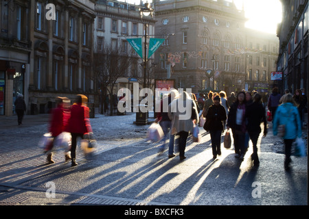 Urban Christmas Shopper stagliano in strade trafficate di Dundee, centro città, Tayside, Scotland, Regno Unito. Silhouette di persone contro il basso sole invernale. Foto Stock