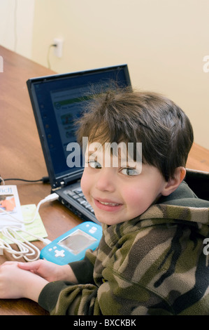 Quattro e 1/2 anno vecchio ragazzo ispanico connette il suo Digi gioco portatile ai suoi genitori computer per caricare programmi. Modello rilasciato. Foto Stock