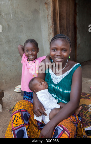 Una giovane madre e i suoi due figli siedono insieme sulla loro veranda in Port Loko, Sierra Leone, Africa occidentale. Foto Stock