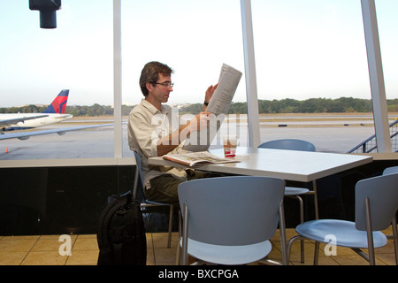 Uomo che legge il giornale e bere il caffè in attesa del volo nel terminal aeroportuale, l'Aeroporto Internazionale di Tampa, Florida, Stati Uniti d'America Foto Stock