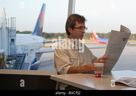 Uomo che legge il giornale e bere il caffè in attesa del volo nel terminal aeroportuale, l'Aeroporto Internazionale di Tampa, Florida, Stati Uniti d'America Foto Stock