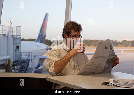 Uomo che legge il giornale e bere il caffè in attesa del volo nel terminal aeroportuale, l'Aeroporto Internazionale di Tampa, Florida, Stati Uniti d'America Foto Stock