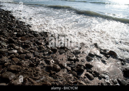 Luccicante onde su una spiaggia rocciosa Foto Stock