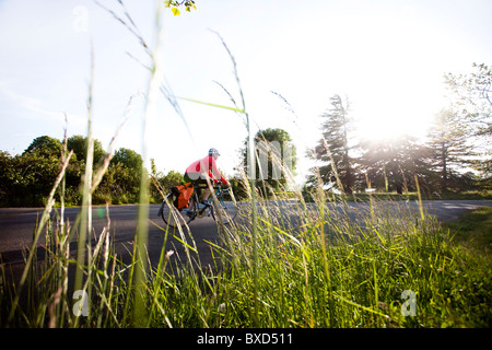 Una giovane donna vanno in bicicletta intorno a un parco al tramonto. Foto Stock