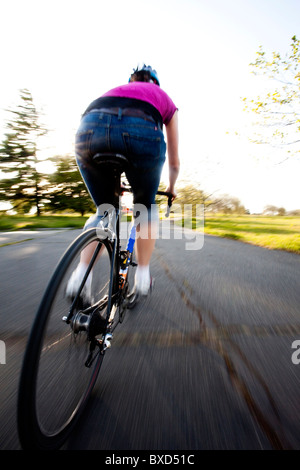 Una giovane donna vanno in bicicletta intorno a un parco al tramonto. Foto Stock