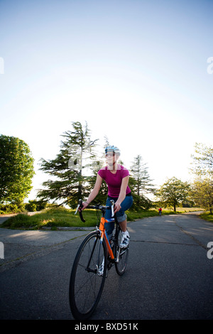 Una giovane donna vanno in bicicletta intorno a un parco al tramonto. Foto Stock