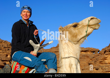 Femmina di equitazione turistica orgogliosamente in un Mehari dromedario durante un escursione in montagna Acacous, il deserto del Sahara, Libia Foto Stock