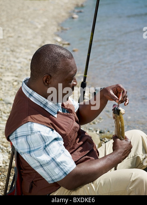 Uomo nero rimozione di pesce dal gancio vicino torrente Foto Stock