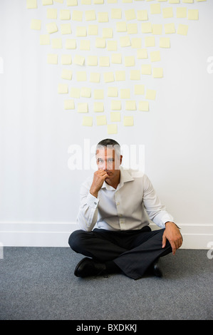 Imprenditore seduto dietro la parete ricoperta in sticky notes Foto Stock