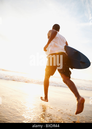 Uomo nero in esecuzione con la tavola da surf in spiaggia Foto Stock