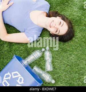 Donna sdraiata su prato accanto al contenitore di riciclaggio Foto Stock