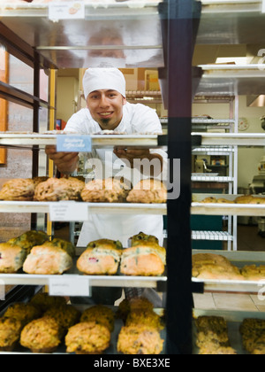 Baker in piedi dietro i vassoi di beni cotti al forno Foto Stock