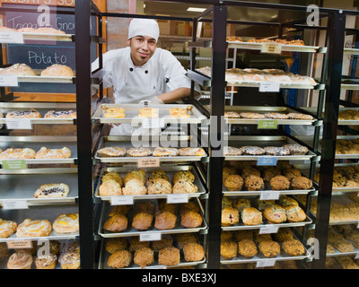 Baker in piedi dietro i vassoi di beni cotti al forno Foto Stock